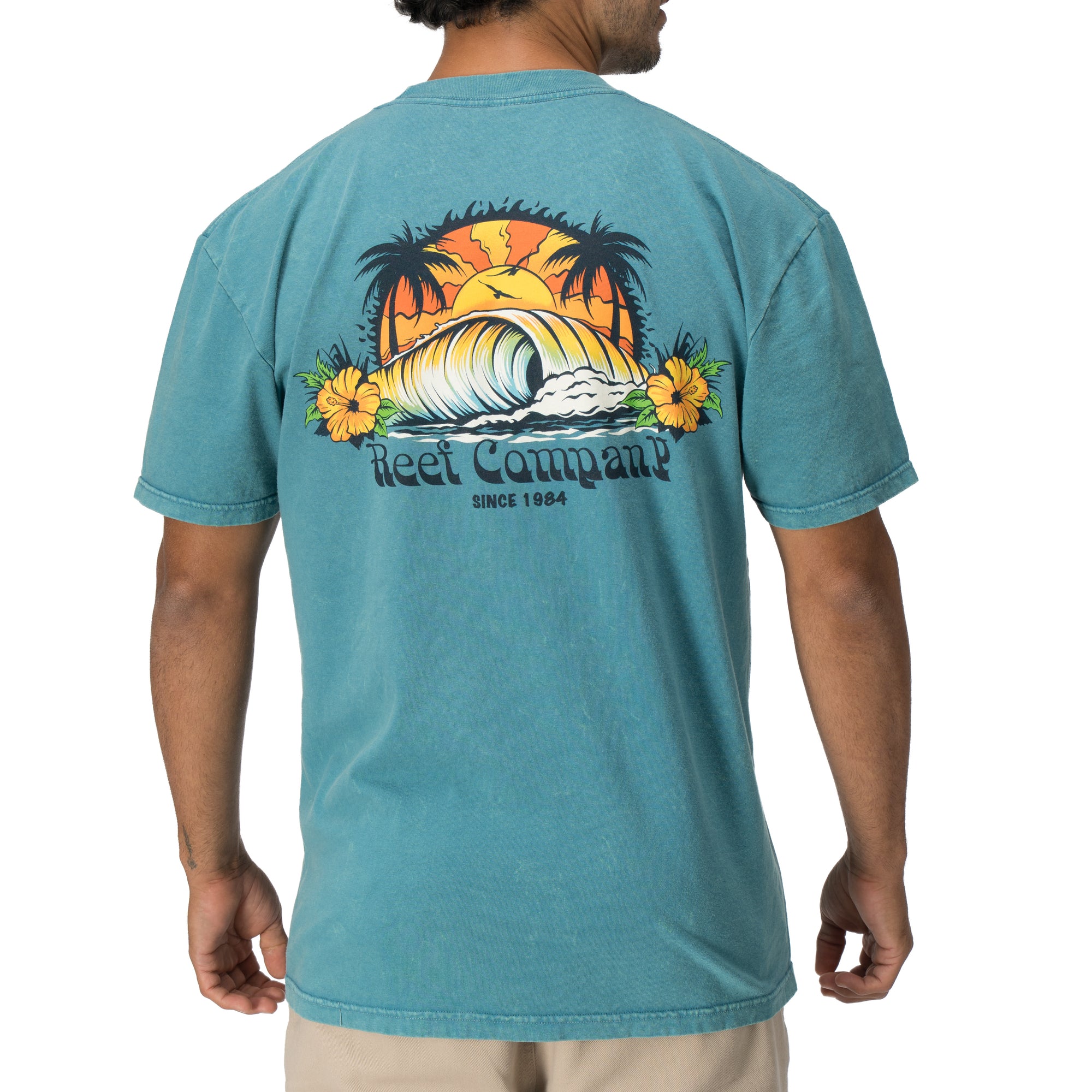 Man wearing Kyle Short Sleeve Tee facing away showing vintage surf wave graphic with palm trees, beach-inspired apparel.