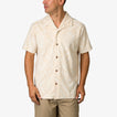 Man wearing a beige Novak Camp Shirt with subtle leaf patterns, front buttoned, facing left in a relaxed pose