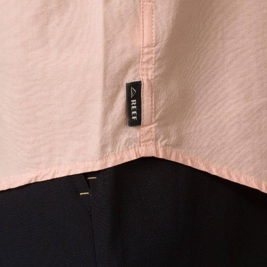 Close-up of the hem and REEF label on the Collins Ss Woven Shirt in soft peach, showcasing surf-inspired apparel detail.