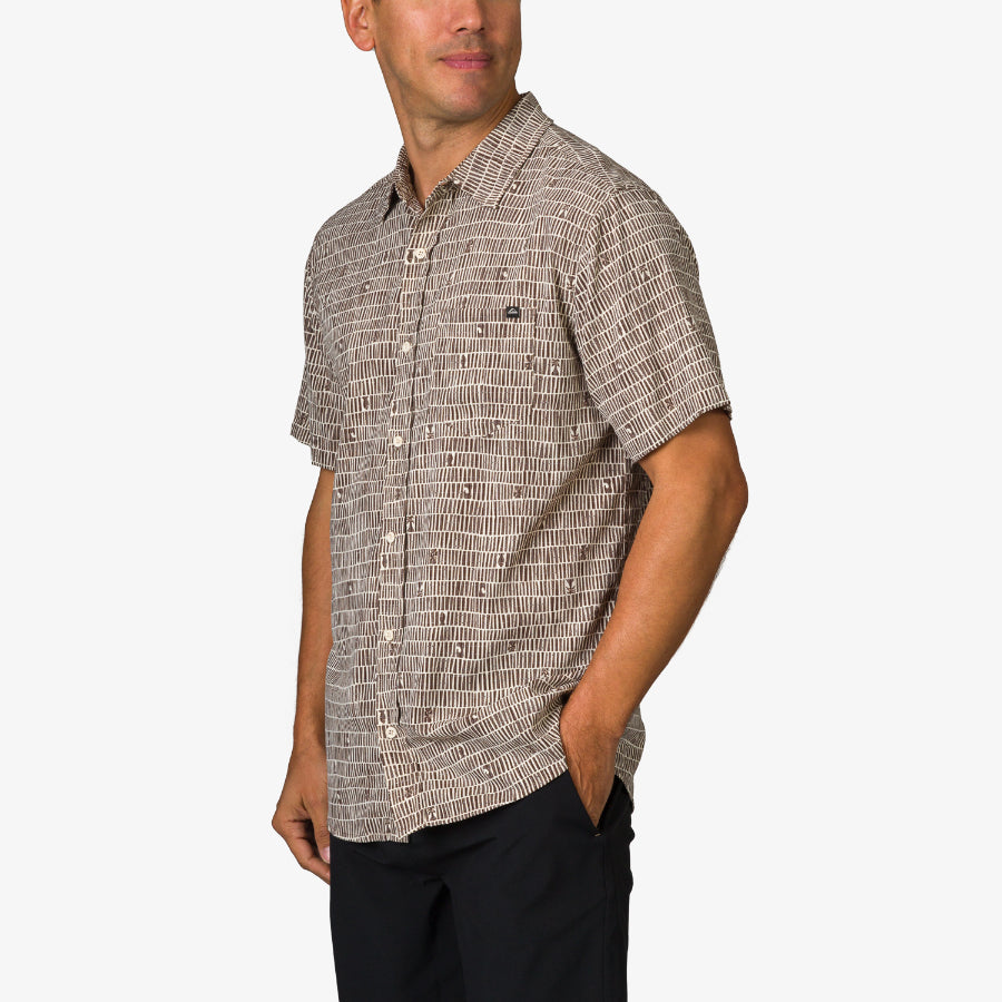 Man wearing Ferris Classic Shirt with beige patterned fabric, short sleeves, and black pants, showcasing casual beach style apparel.