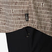 Close-up of the hem of the Ferris Classic Shirt showing surf-inspired brown pattern and REEF tag over black fabric.