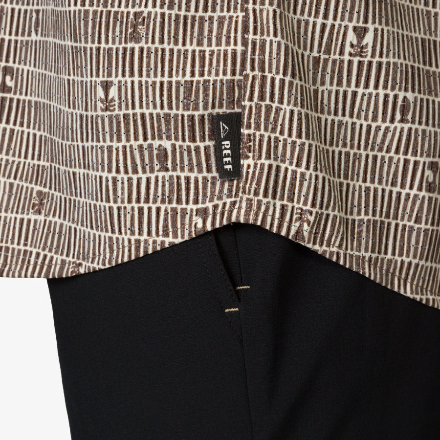 Close-up of the hem of the Ferris Classic Shirt showing surf-inspired brown pattern and REEF tag over black fabric.