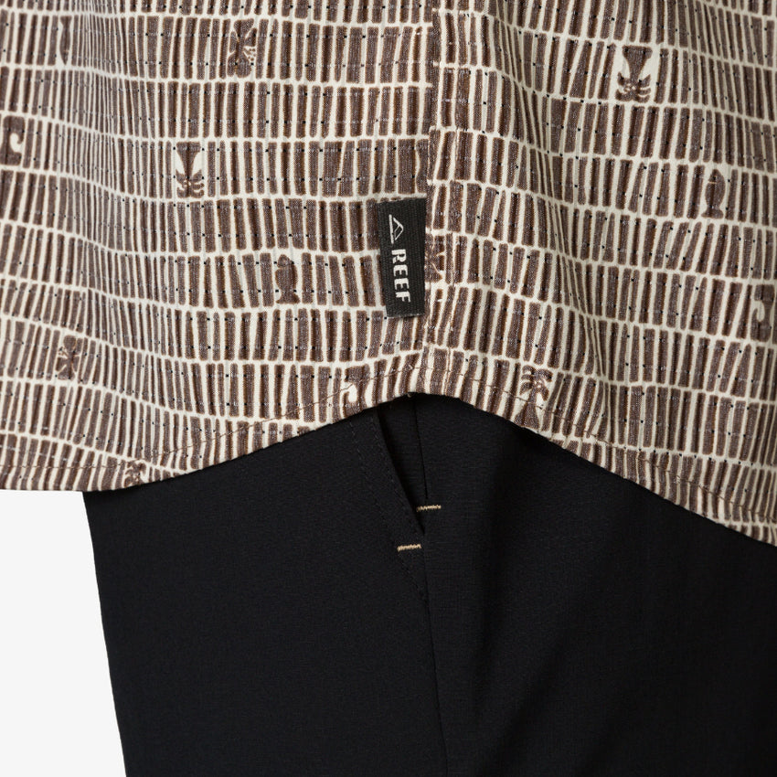 Close-up of the hem of the Ferris Classic Shirt showing surf-inspired brown pattern and REEF tag over black fabric.