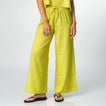 Woman wearing bright green Ollie Pant with loose fit, shown front view from waist to feet in black flip flops facing forward.