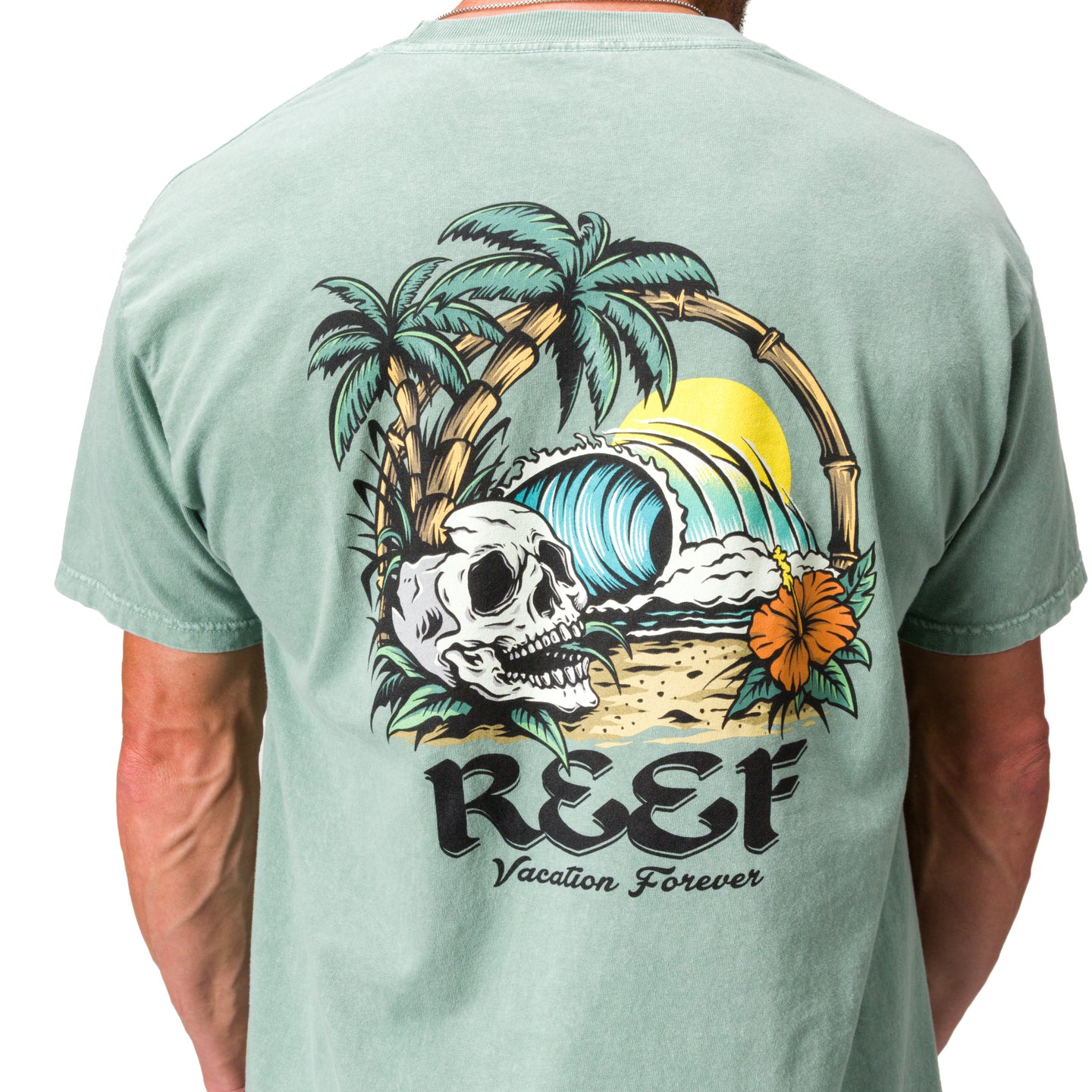Akin Tee on a man, back view, featuring a beach graphic with palm trees, waves, a skull, and reef branding.