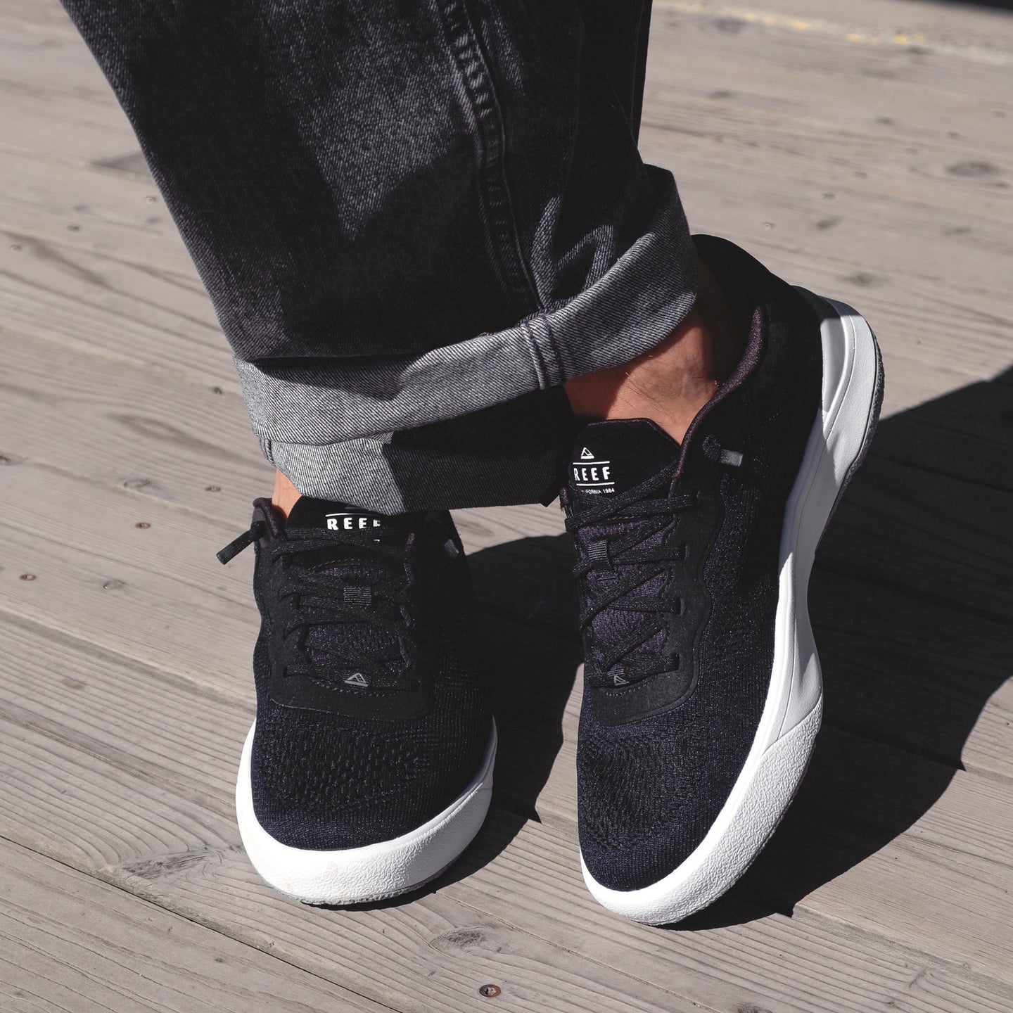 Pair of Shoreline Del Mar sneakers facing forward on wooden deck, highlighting black sustainable design and cushioned comfort.