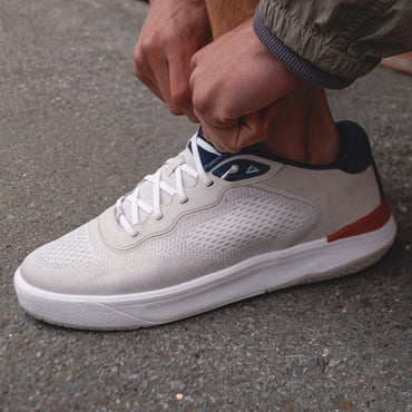 Shoreline Del Mar sneaker facing right, breathable tan knit upper with navy collar, white sole, tying elastic laces.