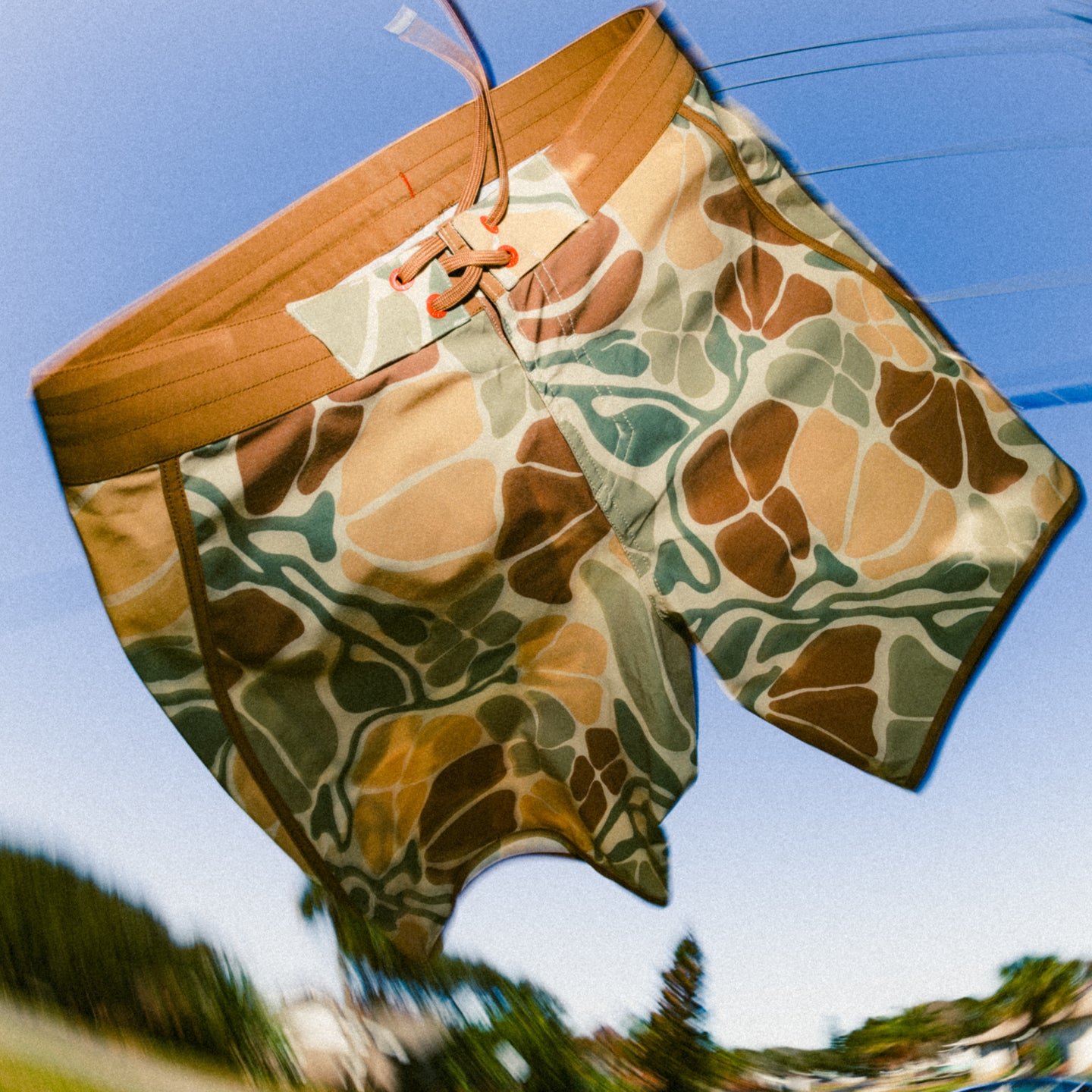 Men's Palmera Boardshort - Floral Camo shown hanging outdoors against blue sky, lightweight water-friendly design for beach use