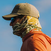 Man facing left wearing Bamboo Lightweight Sun Mask - Floral Camo with tan hat, sunglasses, and orange shirt in bright sunlight