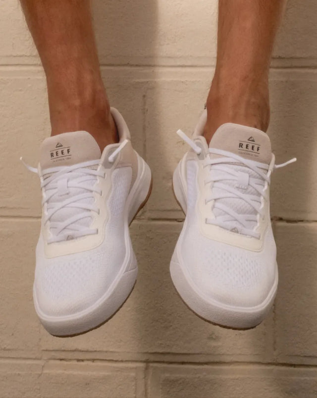 Pair of right-facing white REEF sneakers with mesh upper and laces, shown from front on neutral background