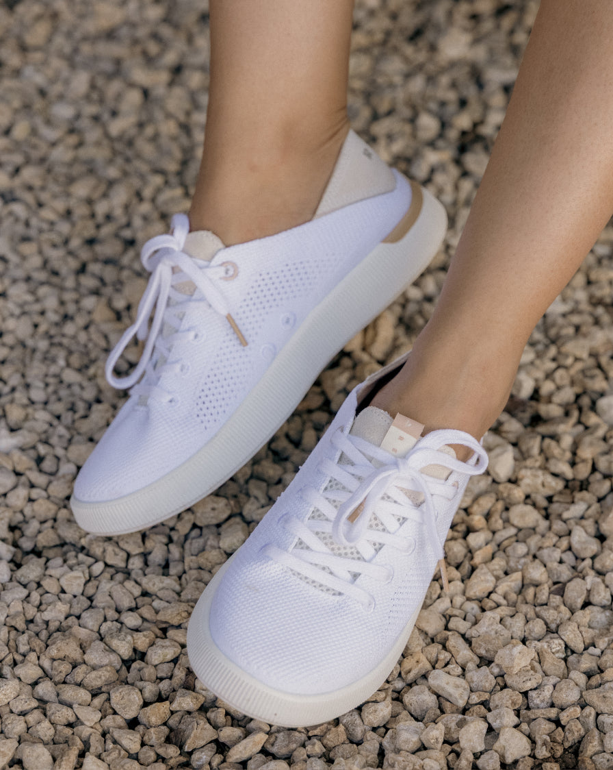 Close-up of feet wearing white REEF sneakers facing forward with breathable knit uppers on rocky ground background