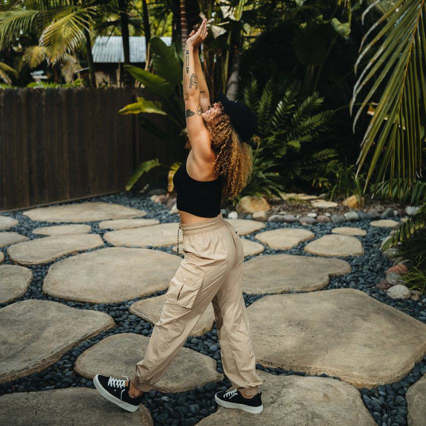 Woman in black crop top and black right-facing sneakers wearing beige Cargo Jogger Pant stretching outdoors on stone path