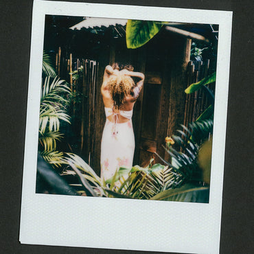 Woman wearing Belladona Dress facing away surrounded by tropical plants in a relaxed outdoor setting