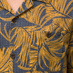 Close-up of men’s Kantis Shirt pocket and buttons with brown tropical leaf print on textured fabric, surf-inspired comfort.