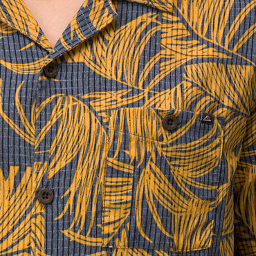 Close-up of men’s Kantis Shirt pocket and buttons with brown tropical leaf print on textured fabric, surf-inspired comfort.