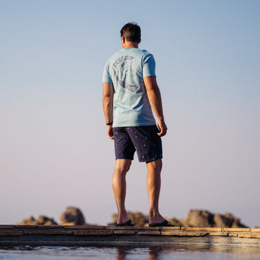 Man wearing La Loca Tee facing away, standing on beach pier with surf-inspired comfort and water-friendly design.