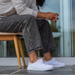 Side view of white Neptune HT sneaker on person seated, featuring lightweight, cushioned, water-friendly design with arch support.