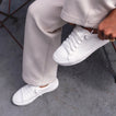 Top view of Lay Day Lite white sneaker on left foot with right foot held up, showing lightweight, breathable upper and arch support.