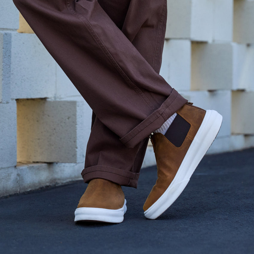 Evo mid-cut brown leather-look shoe facing right, worn with cuffed pants on outdoor pavement, comfort and style blend.