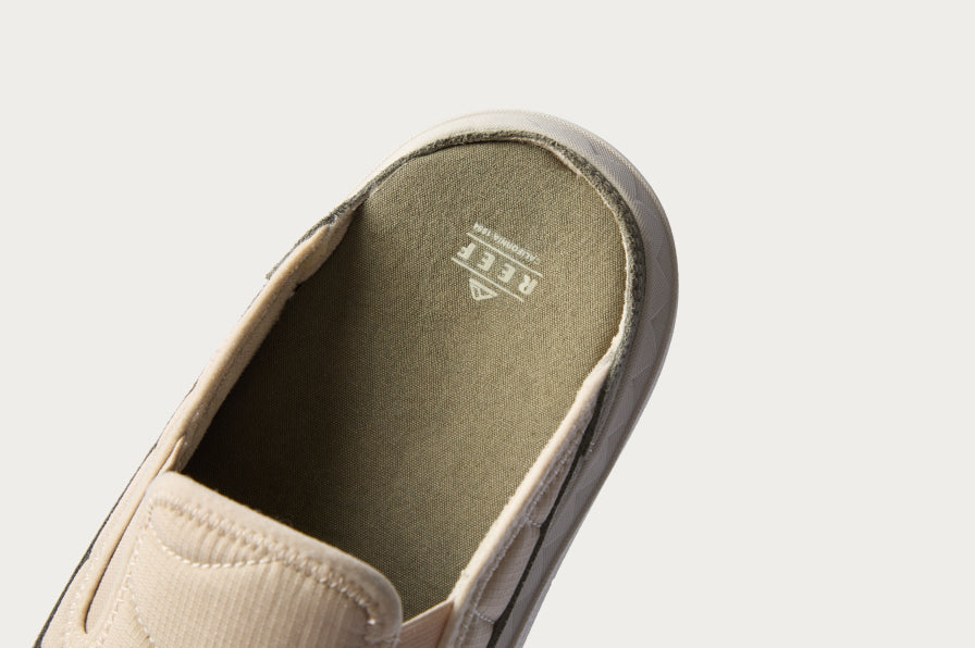 Close-up of the heel area of a beige slip-on shoe facing upward showing cushioned footbed with REEF logo.