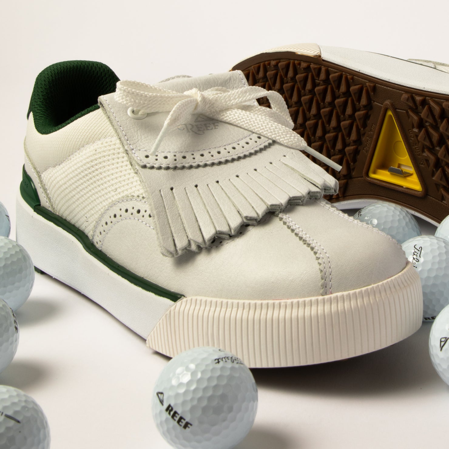 Onshore Pebble men's sneaker facing left, close-up of toe and fringe detail with golf balls on white surface.
