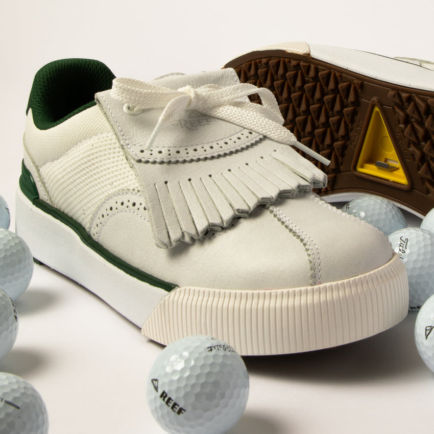 Onshore Pebble men's sneaker facing left, close-up of toe and fringe detail with golf balls on white surface.