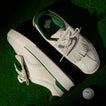 Top and side view of white and green Onshore Pebble men's shoes on green turf with a REEF golf ball nearby