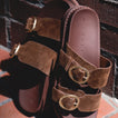 Vista Daphne brown suede slide sandals facing upward with adjustable buckle straps, highlighting soft cushioning and arch support.