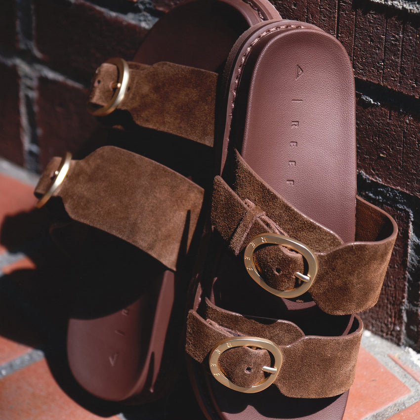 Vista Daphne brown suede slide sandals facing upward with adjustable buckle straps, highlighting soft cushioning and arch support.
