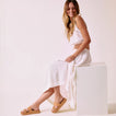 Woman sitting on white block facing left wearing Vista Hi 2 tan sandals with enhanced arch support and cushioned platform