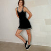 Woman wearing Reef Del Mar shoes facing right, paired with casual black dress with white stripes on hem and straps.