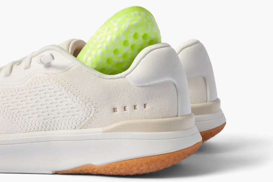 Close-up of the back of white REEF sneakers facing right with a lime green cushioned insert showing comfort features.
