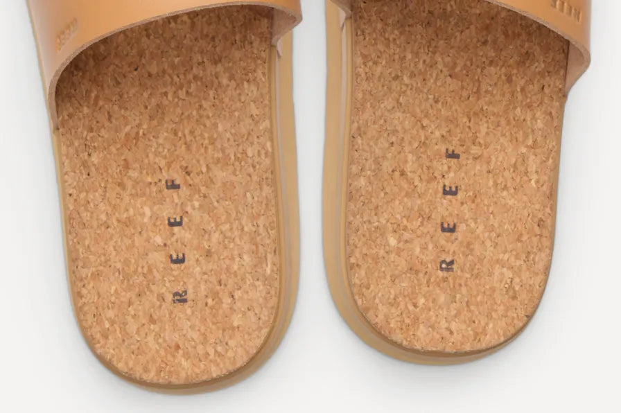 Close-up top view of tan REEF slides showing cork footbeds and soft straps facing upward for beach comfort and support
