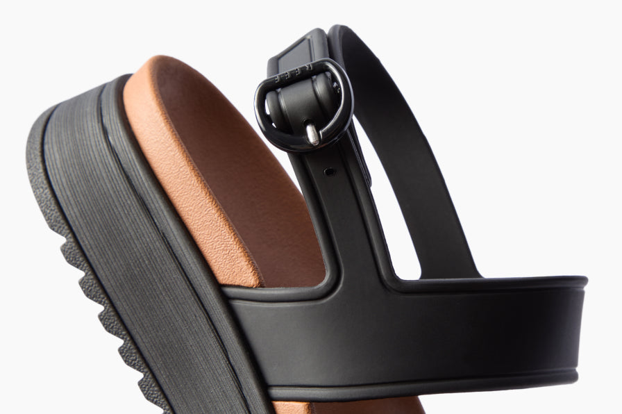 Black platform sandal facing left, shown in side view with an adjustable buckle strap and cushioned footbed