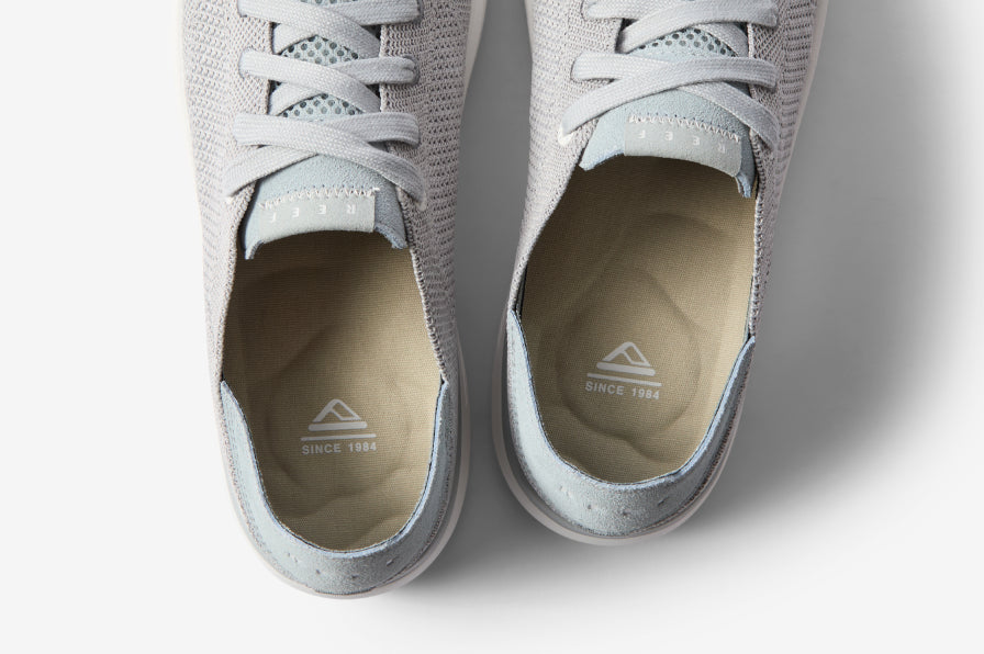 Top-down view of light gray sneakers showing cushioned insoles with brand logo and breathable fabric uppers