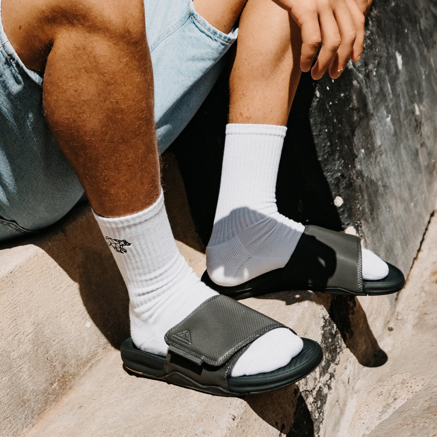 Phantom Slab black slides facing right with cushioned footbeds on a rocky beach