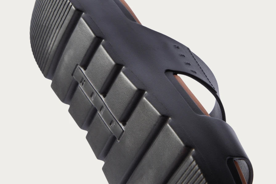Close-up of the bottom sole and side of a black surf-inspired sandal facing left, showing textured grip and cushioning.