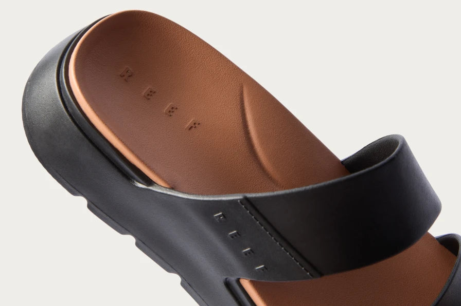 Close-up of the left side of a black REEF slide sandal showing soft-rebound cushioning and molded footbed.