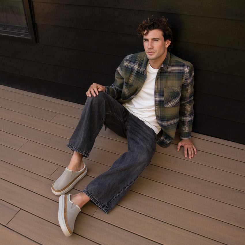 man wearing Rambler Mule Brown and jeans and a flannel sitting outside a cabin