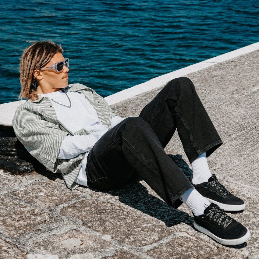 Shoreline Del Mar black sneakers facing right on a seaside pier by the ocean