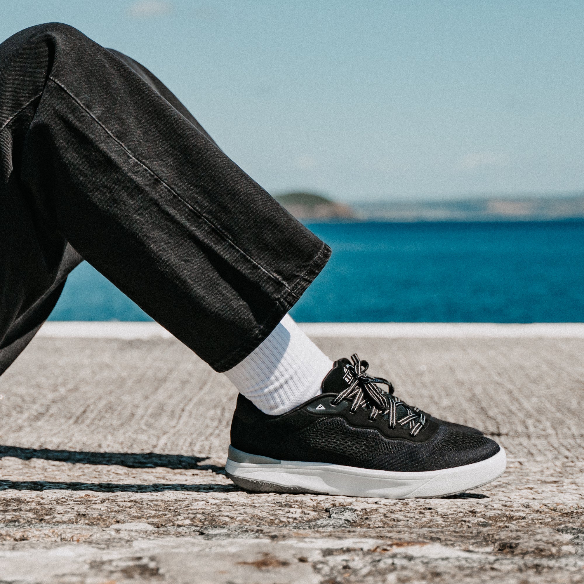 Shoreline Del Mar black sneaker facing right on a beach promenade, showcasing cushioned comfort for everyday wear