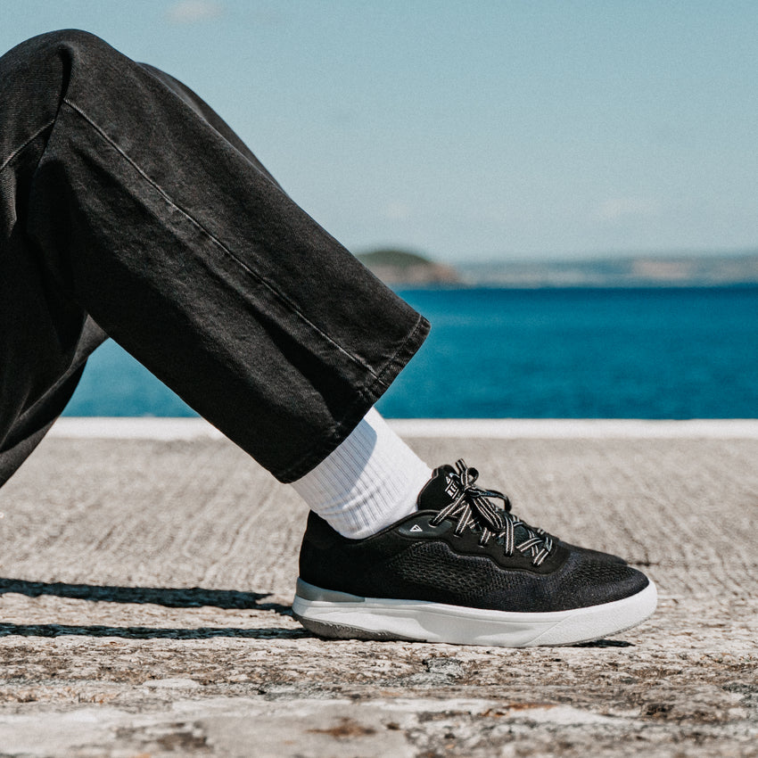 Shoreline Del Mar black sneaker facing right on a beach promenade, showcasing cushioned comfort for everyday wear
