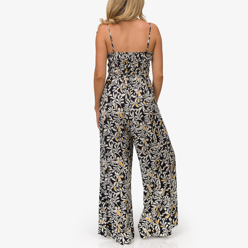 Woman wearing a black floral Sandy Romper shown from the back, featuring lightweight, beach-inspired comfort apparel.