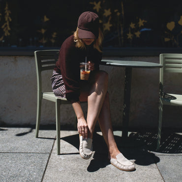 Woman seated outdoors wearing Vista Myra facing left, women's warm sand leather clog with enhanced arch support and soft cushioning