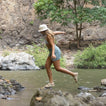 Woman wearing Reef Water Vista sandals facing right, mid-step over rocks by water, showing side view of sandals and arch support.