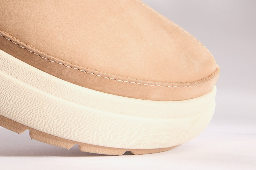 Close-up of tan shoe toe with stitched upper and thick cushioned off-white midsole facing right on neutral background