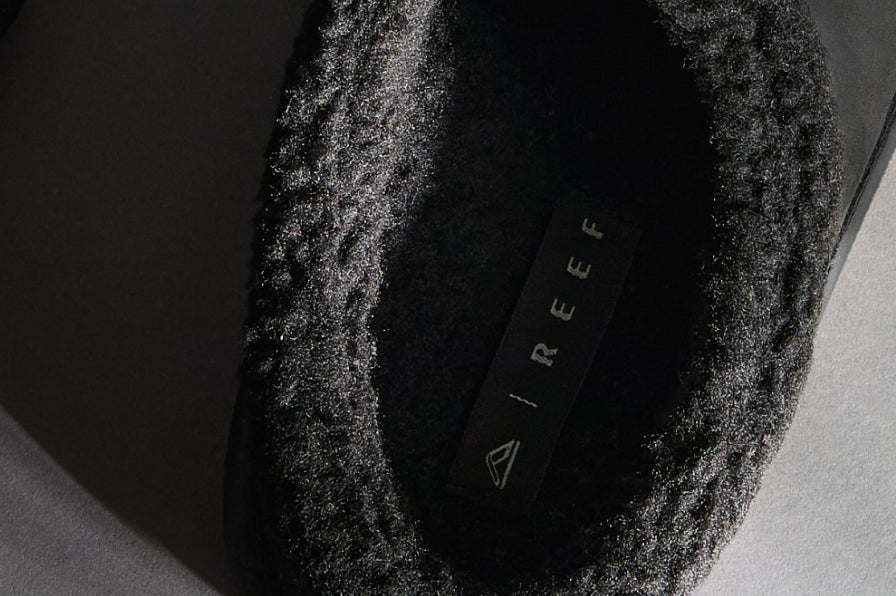 Close-up of black slip-on shoe opening showing soft textured lining and REEF logo on footbed facing upward