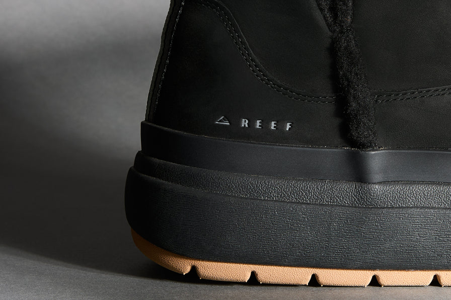 Close-up of black REEF boot heel with textured midsole and gum outsole facing left on neutral background