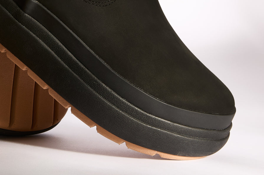 Close-up of black shoe front and sole showing thick cushioned platform with gum tread, facing right on white background