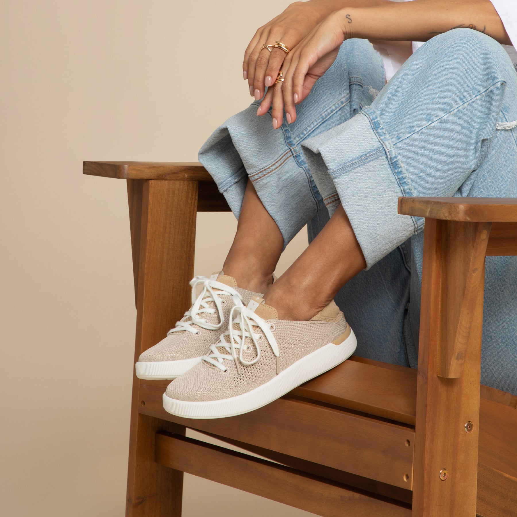 Reef Neptune womens beige slip-on sneaker facing right with soft cushioning and arch support, worn seated in wooden chair.